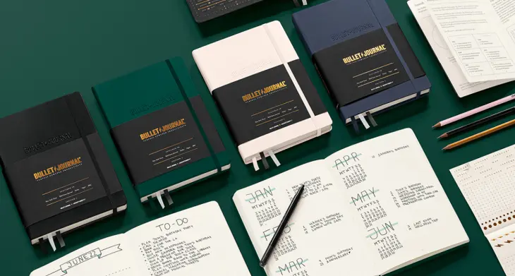 Mehrere Bullet Journals von LEUCHTTURM1917 liegen zugeklappt und aufgeschlagen auf dunkelgrünem Hintergrund.