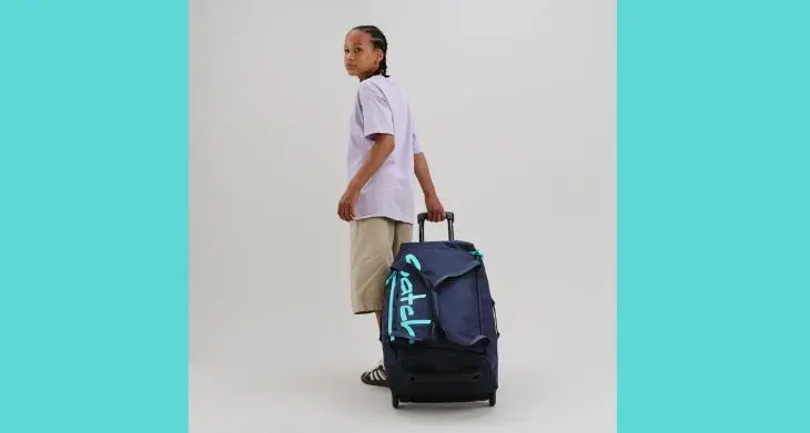 Ein Junge zieht die Reisetasche satch quest hinter sich her