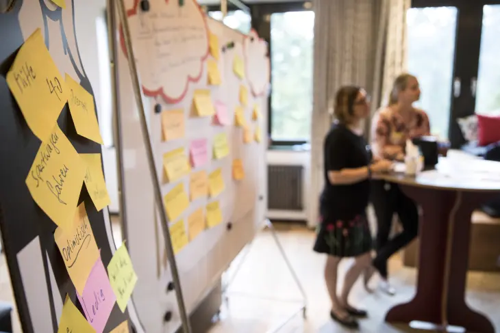 Eine Gruppe sitzt in einem Workshop rund um Metaplanwände, die mit Haftnotizen beklebt sind. 