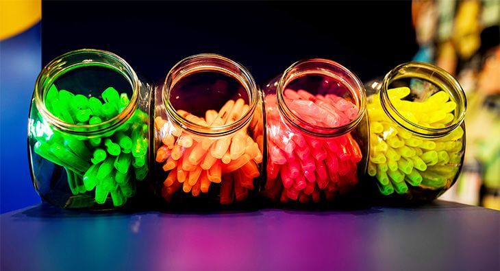 Vier Vorratsgläser aus Glas stehen auf einem blauen Tisch. Sie sind gefüllt mit Textmarkern der Marke Soennecken in den Farben grün, orange, rosa und gelb.