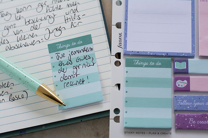 Nahaufnahme einer Seite in einem Terminkalender von Filofax. Man sieht eine beschriebene Seite, ein Kugelschreiber ragt links ins Bild. Auf einer Haftnotiz mit der Überschrift „Things to do“ steht in Handschrift „Tue jemandem etwas Gutes, der gar nicht damit rechnet!“. Im rechten Bildrand sieht man einen Bogen mit sticky notes von Filofax.