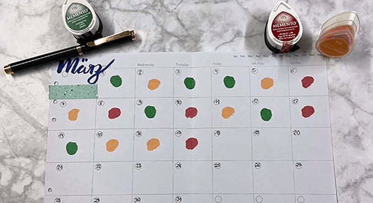 Aus der Vogelperspektive blickt man auf einen aufgeschlagenen Terminkalender, bei dem die Tage mit unterschiedlichen Farben markiert sind.