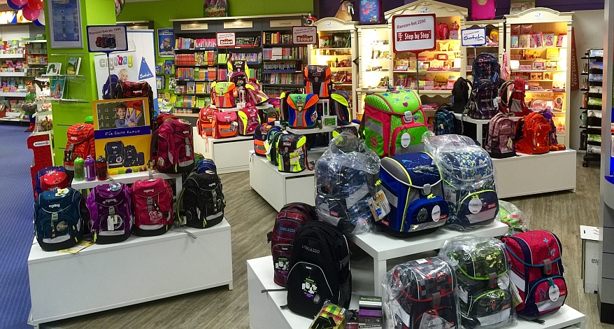 Viele bunte Schulranzen der Marken ergobag, Step by Step und Scout stehen im Regal und davor.