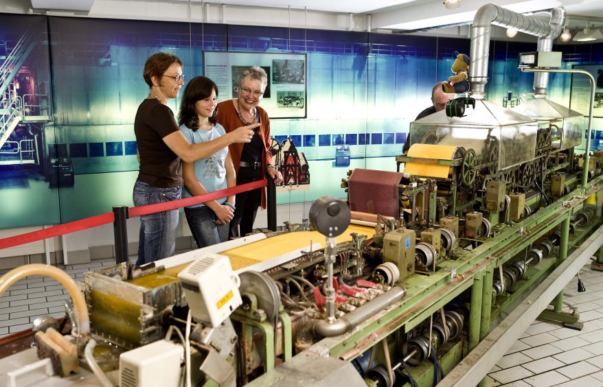 Drei Frauen stehen vor einer Laborpapiermaschine im LVR-Industriemuseum in Bergisch Gladbach.