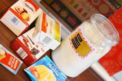 Auf einem Tisch stehen Zutaten zum Backen: Butter, Puddingpulver, Vanillzucker, Puderzucker. In einem Weckglas ist mehr eingefüllt. Auf dem Weckglas sieht man einen Aufkleber, der mit Prägeband und der Aufschrift "Mehl" verzeirt ist.