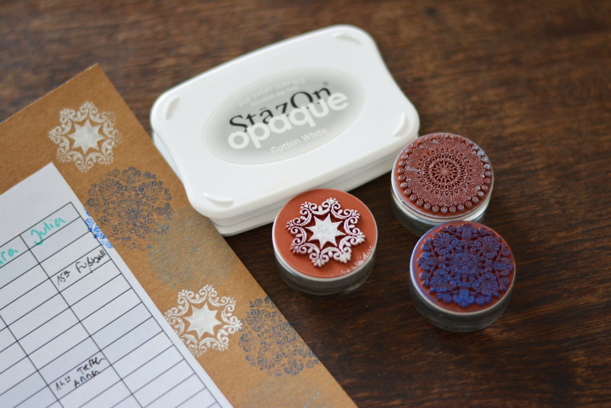 Planer auf braunem Karton mit weißen Stempeln und Deko-Stempeln daneben.