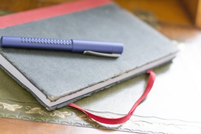 Ein altes abgegriffenes Tagebuch liegt auf einem Sekrtetär. Auf dem Tagebuch liegt ein lila Grip-Füller der Marke Faber-Castell.