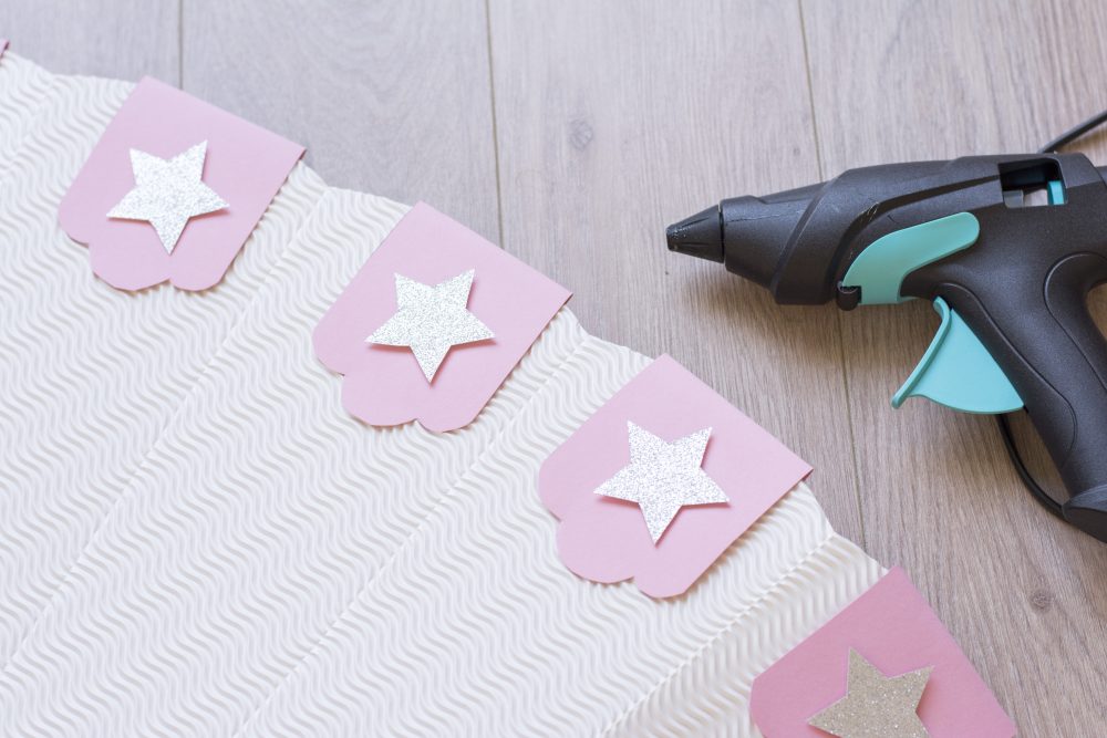 Das obere Ende einer rosa Schultüte liegt auf einem Tisch und ist mit Sternen verziert. Daneben liegt eine Heißklebepistole.