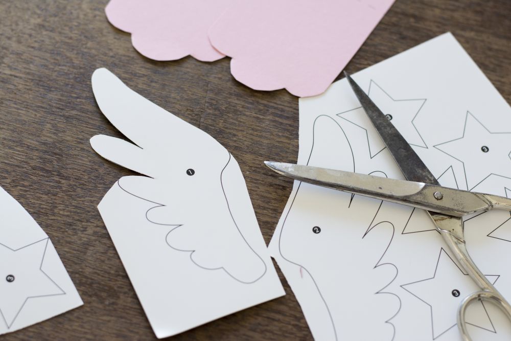 Ein Element des Bastel-Sets liegt halb ausgeschnitten auf dem Tisch. Daneben liegt eien Schrer auf den restlichen Vorlagen.