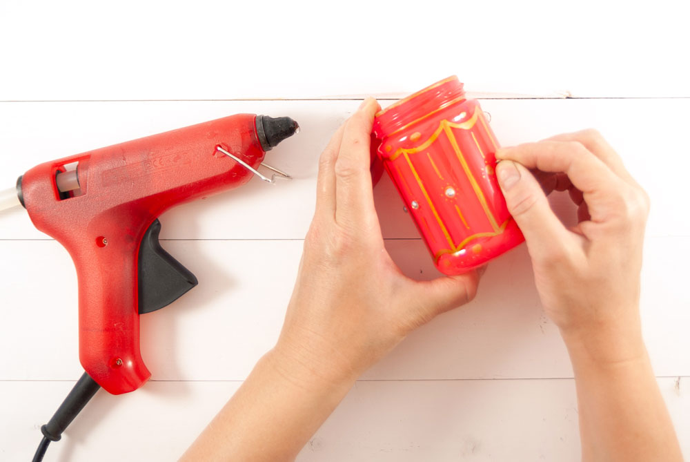 Auf ein rotes Glas mit goldenen Ornamenten werden Pailletten geklebt
