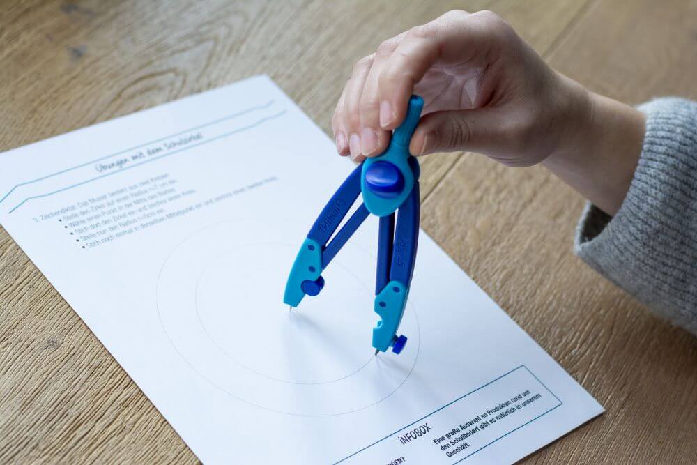 Eine Hand hält den Schulzirkel griffix von Pelikan und führt auf einem Blatt Papier Zirkelübungen aus. 