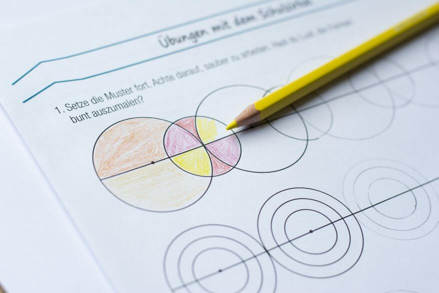 Nahaufnahme eines Übungsblatts zum Thema Zirkelübungen in der Grundschule. Die gezeichneten Kreise werden mit Buntstiften farbig ausgemalt.