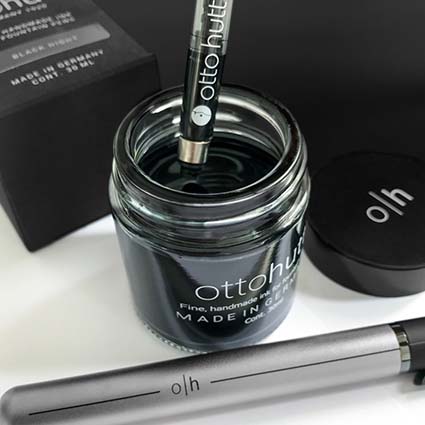 Ein Konverter wird mit schwarzer Tinte der Marke Otto Hutt aus einem Tintenglas gefüllt. Vor dem Glas liegt ein Füller der Marke Otto Hutt. 