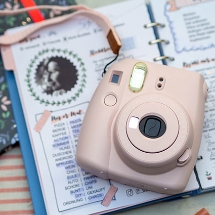 Auf einem hellgrauen Untergrund liegt ein aufgeschlagenes Clipbook von Filofax. Auf den Seiten ist ein Teil eines ausgefüllten Freundebuches für Erwachsene zu sehen. darauf liegt eine hellrosa Sofortbildkamera. Foto: Johanna Rundel