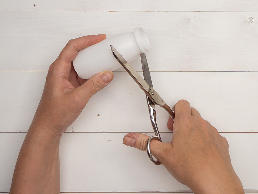 Jemand schneidet eine kleine, weiße Plastikflasche mit einer Schere am „Hals“ auseinander. Der Untergrund ist hell. Foto: Johanna Rundel