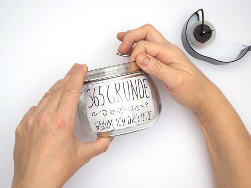 Jemand legt ein mit einem Schriftzug bedrucktes Papier an die innere Wand eines Vorratsglases. Foto: Johanna Rundel