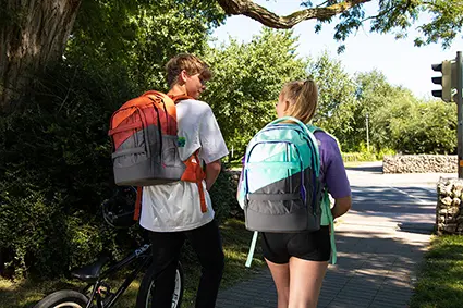 Ein Junge und ein Mädchen im Teenageralter laufen durch eine Allee. Beide tragen Schulrucksäcke von satch und unterhalten sich miteinander.