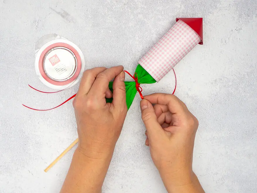 Jemand bindet das Krepppapier einer selbstgebastelten Silvesterrakete mit einem dünnen, roten Satinband von KNORR prandell zusammen. Foto: Johanna Rundel 