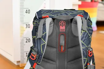 Ein schwarzer Schulranzen von Step by Step steht vor einem Maßstab. Man sieht das Tragesystem und die Verstellmöglichkeiten auf der Rückseite.