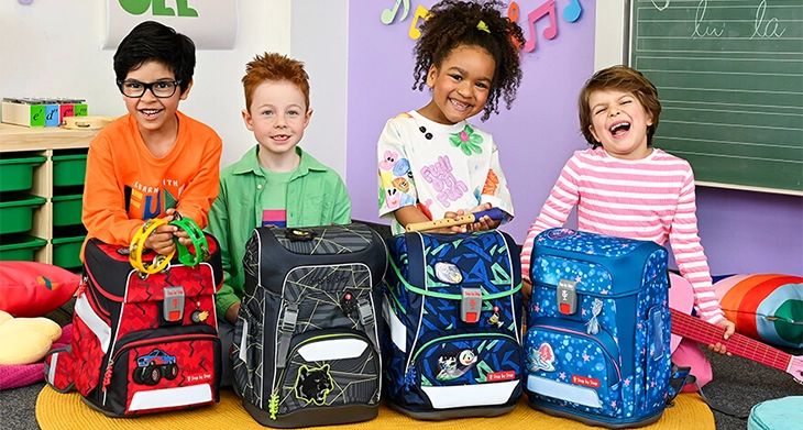 Vier Grundschulkinder hocken in einem Klassenraum hinter ihren unterschiedlichen Schulranzen von Step by Step.