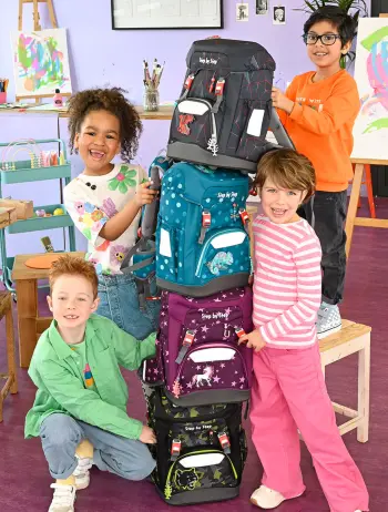 Vier Grundschulkinder haben einen hohen Turm aus ihren Schulranzen von Step by Step gebaut und stehen lachend darum.