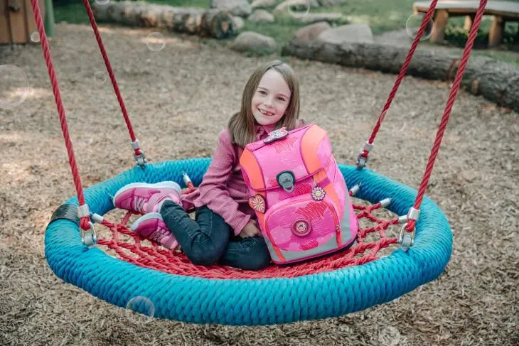 Ein Mädchen sitzt mit einem Schulranzen von DerDieDas in einer Nestschaukel.