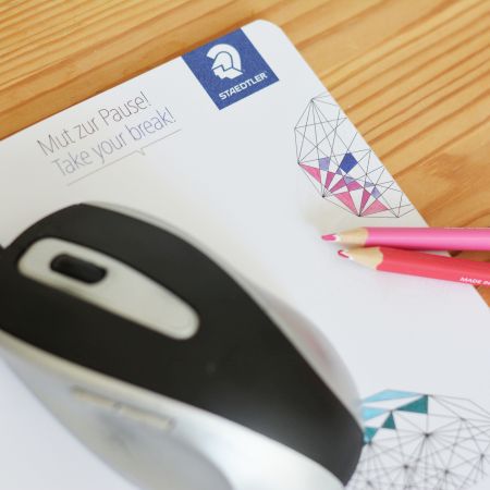 Auf einem Block der Marke Staedtler liegen 2 Bunstifte, mit denen Muster auf dem Block ausgemalt wurden. Auf dem Block liegt eine Computermaus.
