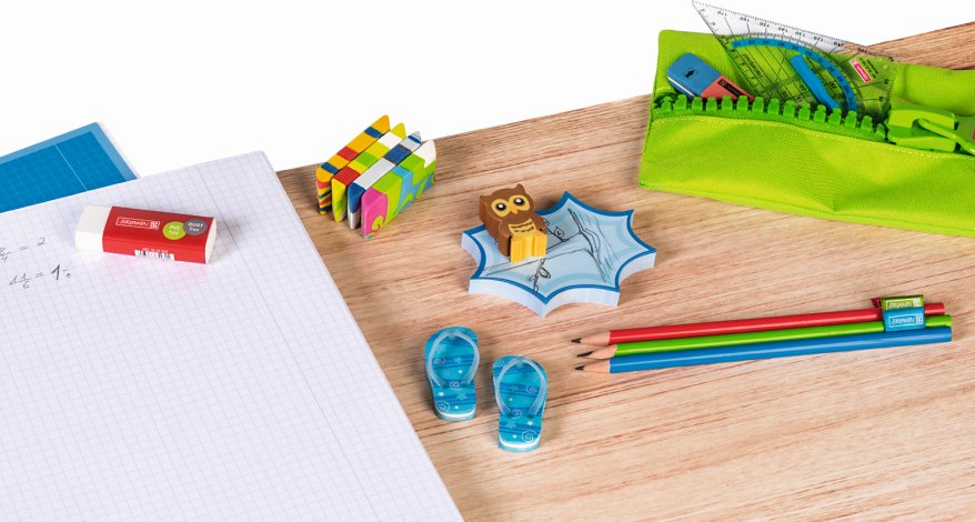 Auf einem Tisch liegen bunte Radiergummis, Bleistifte, ein karrierter Collegeblock und ein Stiftemäppchen der Marke Brunnen.