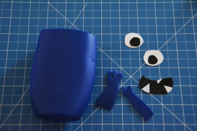 Auf einer Schneidematte liegen die Einzelteile einer leeren blauen Shampooflasche, aus der ein Monster gebastelt werden soll.