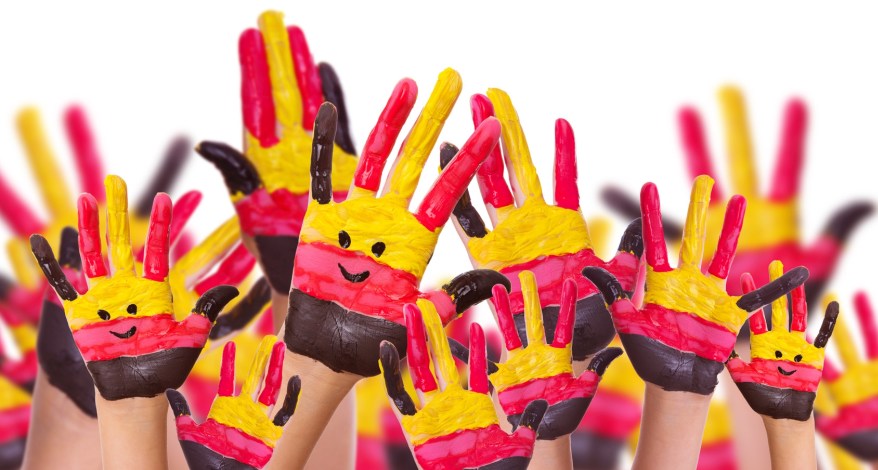 Ganz viele Hände, die in die Höhe gestreckt sind und in den Farben der deutschen Nationalflagge bemalt sind und Gesichter haben.