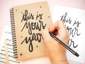 Jemand lettert den Spruch „this is your year“ mit einem schwarzen Stift auf einen Schülerkalender aus Kraftkarton von BRUNNEN. Foto: Johanna Rundel