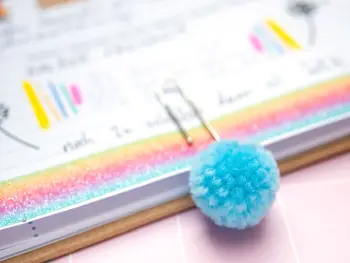 Eine Büroklammer, an der ein Pompon befestigt ist (KNORR prandell) steckt in einem Schülerkalender von BRUNNEN. Foto: Johanna Rundel