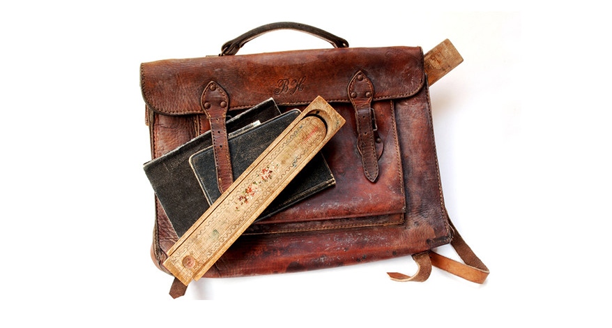 Abbildung eines alten Lederschulranzens, auf dem 2 alte Schulhefte liegen.