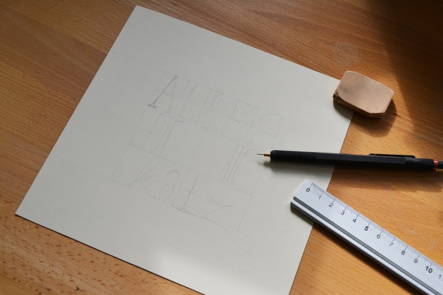 Auf einem Blatt Papier ist der Schriftzug "Alles für die Katze" in ein Raster gezeichnet. Daneben liegen ein Lineal, ein Stift der Marke Rotring und ein Radiergummi.