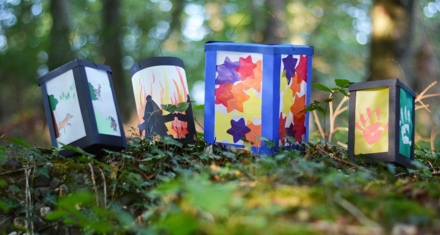 Auf einem Waldboden stehen mehrere, aus buntem Transparentpapier gebastelte Laternen.