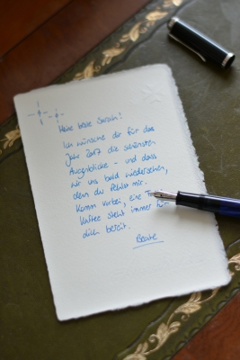 Auf einer leder-Schreibtischunterlage liegt ein handgeschriebener Brief. Der Brief wurde mit Füller und blauer Tinte geschrieben, der geöffnete Füller liegt auf dem Briefpapier und die Kappe des Füllers daneben.