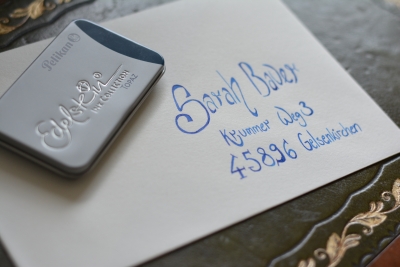 Nahaufnahme des beschrifteten Briefumschlags. Darauf liegt eine Metallbox von Pelikan mit Edelstein-Tintenpatronen.