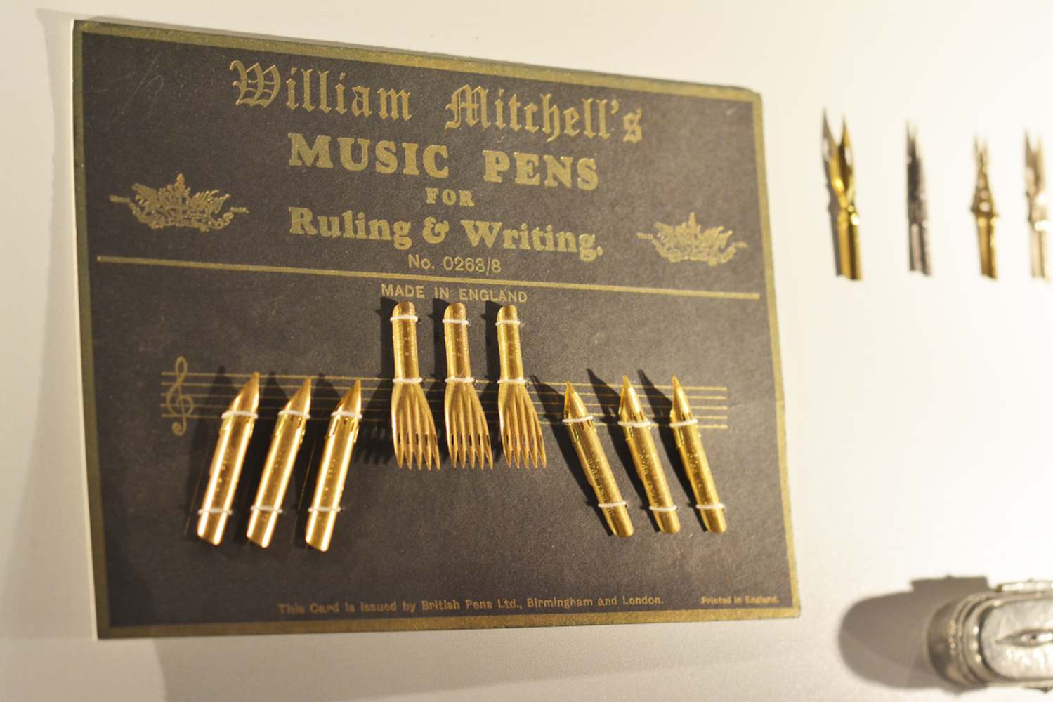 Schild mit dem Text "William Mitchell's Music Pens for Ruling & Writing". Darunter sind 3 verschiedeneArten von Schreibfedern angebracht.
