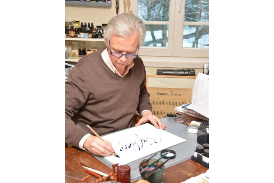 Martin Heickmann sitzt in seinem Museum am Schreibtisch und kalligrafiert etwas auf einem Blatt Papier.