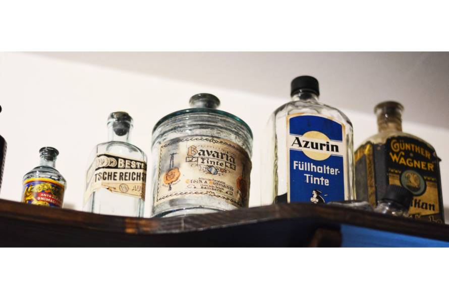 Auf einem Schrank stehen diverse leere alte Flaschen, in denen einmal Tinte drin war.