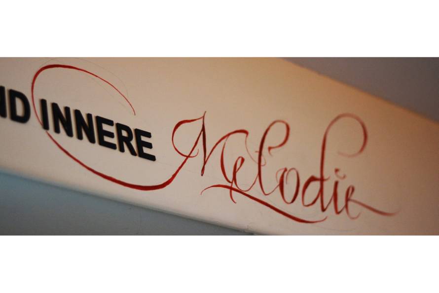 Ausschnitt eines Satzes, bei dem das Wort "Melodie" mit roter Tinte kalligrafiert ist.