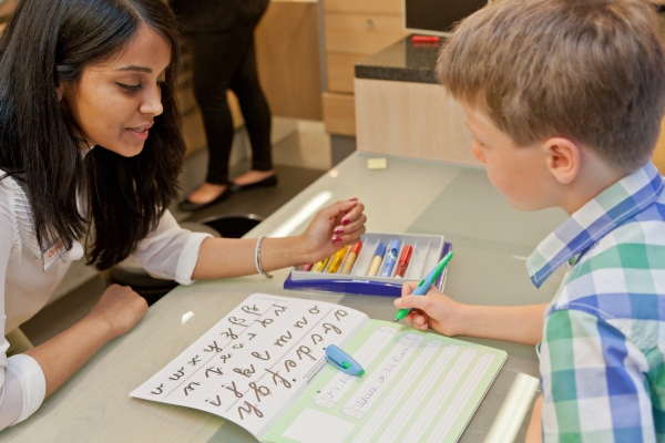 Eine Frau sitz mit einem Jungen vor einem Schreiblernheft.