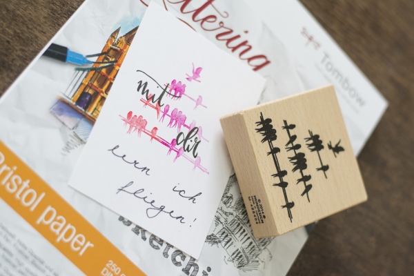 Karte mit rosa Vogelstempel und Schriftzug „mit dir… will ich fliegen!“ liegen auf einem Tombow Papierblock.