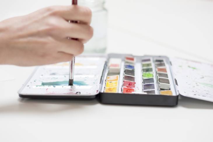 Hand taucht Pinsel in Aquarellfarben-Palette für DIY-Projekt