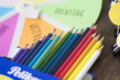 Buntstifte der Marke Pelikan liegen, aufgefächert in der Verpackung, auf dem selbstgebastelten Wochenplan für Kinder. 