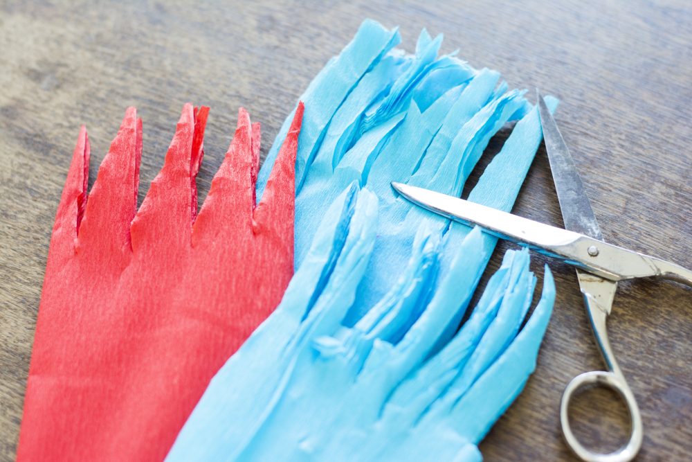 rotes und blaues Krepppapier, welches am Ende zackig geschnitten wurde, leiegn auf einem Holztisch.