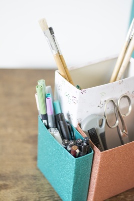 Ein Organizer aus beklebten Müslikartons, der mit Pinseln und Bastelmaterial gefüllt ist.