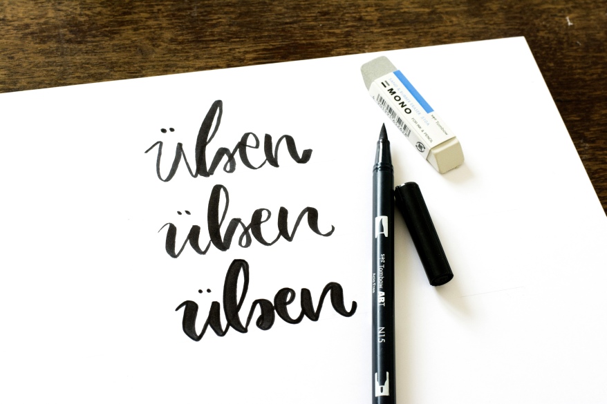 Handlettering-Übung mit dem Wort "üben" mit Brushpen und Radiergummi auf Papier