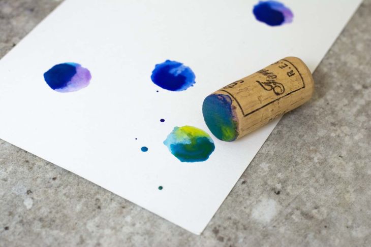 Weinkorken stempelt blau-grüne Farbverläufe auf weißes Papier.