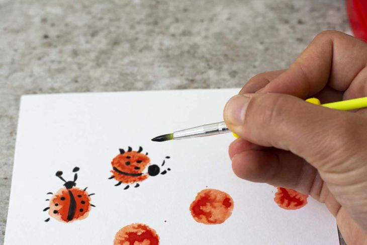 Eine  Hand zeichnet Details an gestempelte Marienkäfer auf Papier.